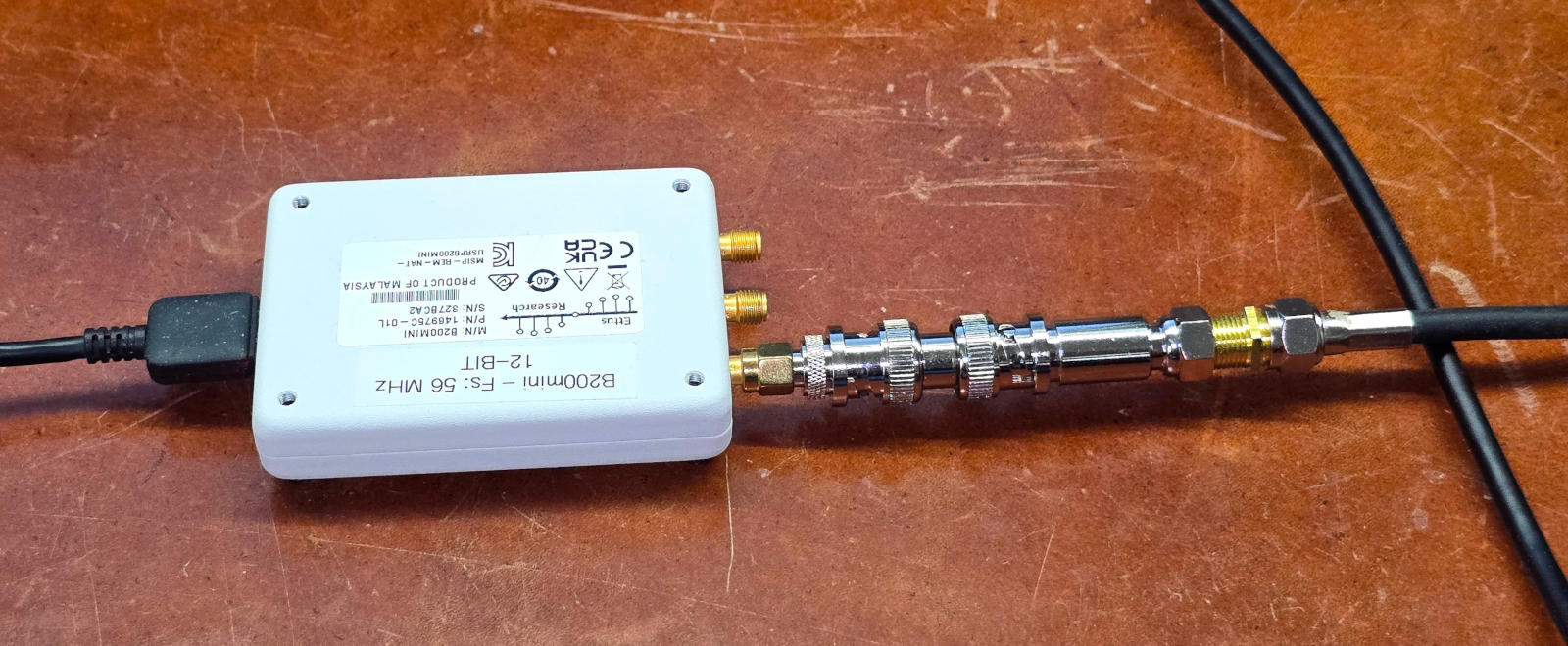A topview of a small software defined radio a few centimeters per side and connected to a USB cable on the left and a coaxial cable on the right.