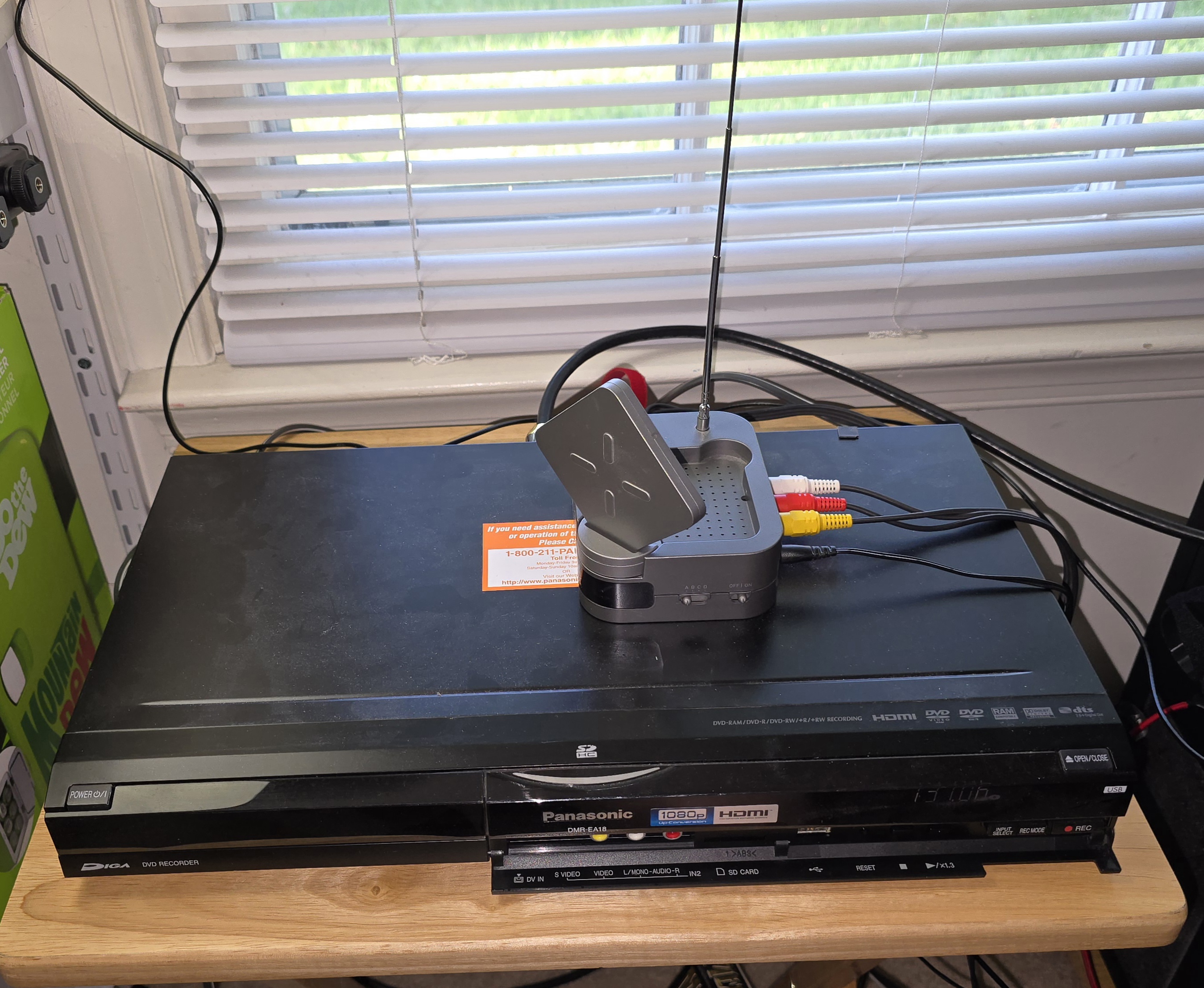 Image showing a wide DVD player with a small, gray box on top. The gray box roughly 5 cm square and 3 cm high has three colored connectors plugged into it, a yellow, red, and white one. Out of the top of the gray box extends a thin wire antenna roughly 20 cm long.
